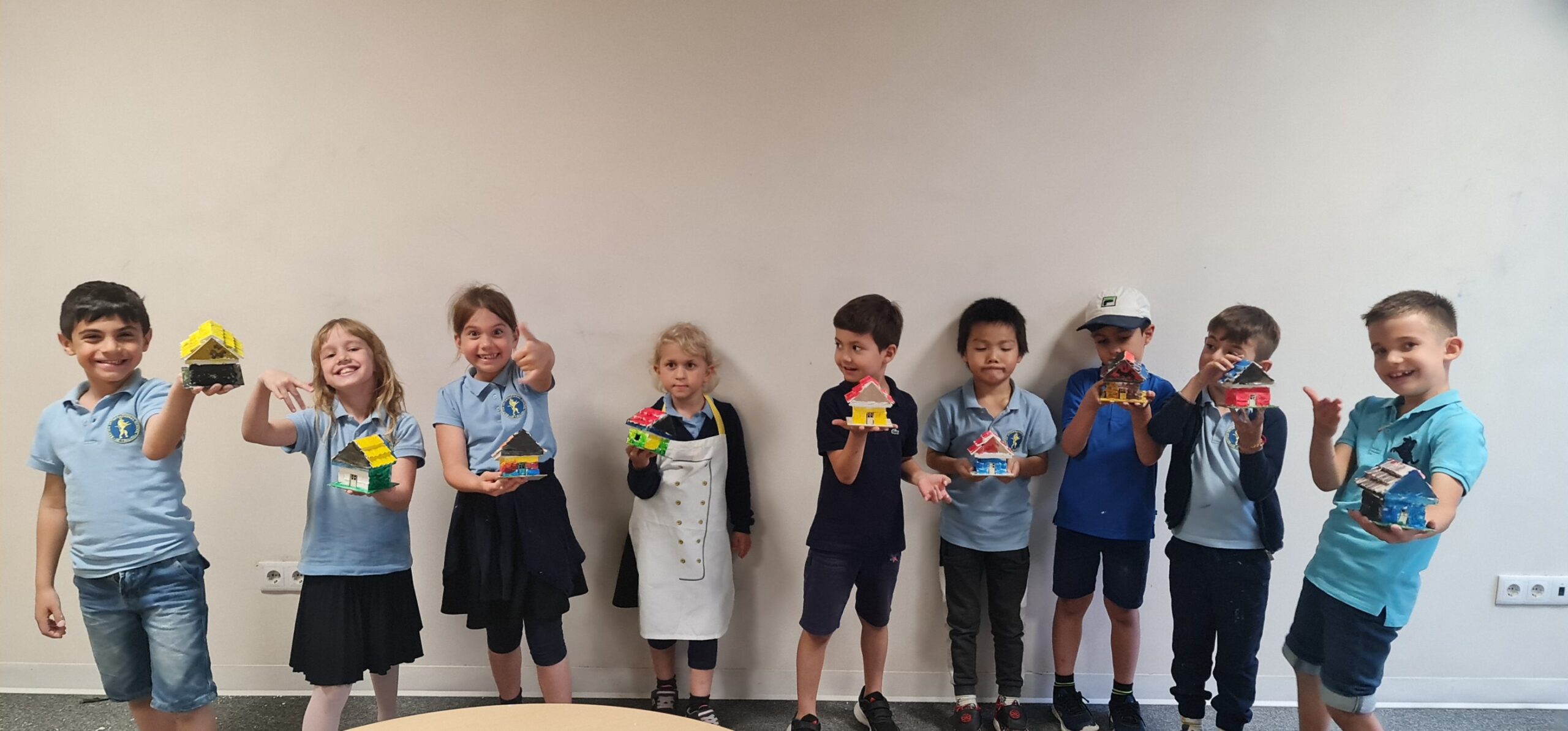 Colorful kids holding handmade craft houses at school.